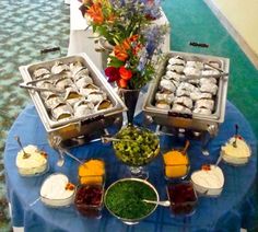 several trays of food on a blue table cloth with flowers in vases behind them