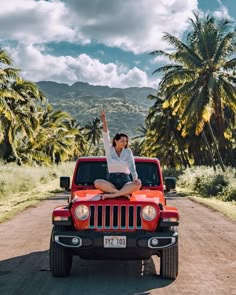 a woman sitting on the back of a red jeep with palm trees in the background