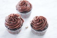 three cupcakes with chocolate frosting and nuts on a white tablecloth, top view