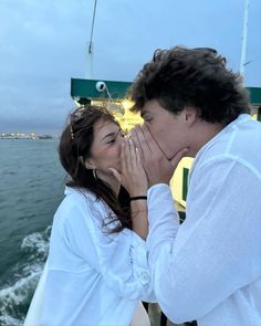 a man and woman kissing while on a boat in the water with their hands covering their mouths