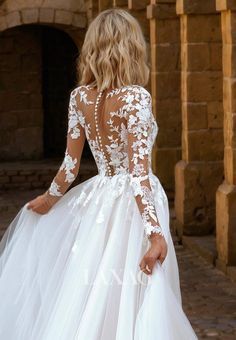 a woman in a white wedding dress standing on a stone walkway with her back to the camera