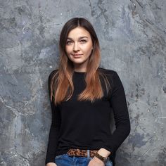 a woman standing in front of a wall with her hands on her hips and looking at the camera