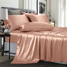 a bed with pink sheets and pillows on top of it, next to a night stand