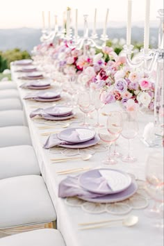 a long table is set up with purple and white plates, napkins and wine glasses