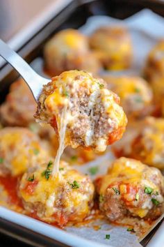 a spoon full of meatballs with cheese and sauce on them, being lifted from a casserole dish