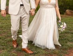 a bride and groom hold hands as they walk through the grass