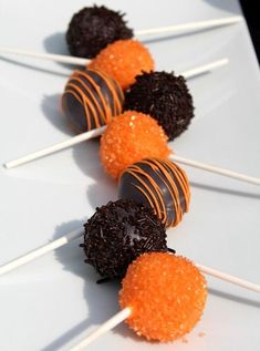 several orange and black candies on sticks with sprinkles sitting on a white plate