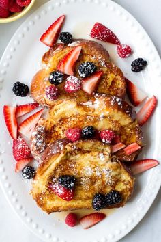 french toast with berries and powdered sugar on a white plate next to a bowl of strawberries