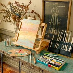 an easel, paintbrushes, and other art supplies sit on a table