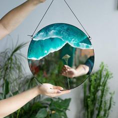 a person holding up a mirror with an image of a wave in the ocean on it