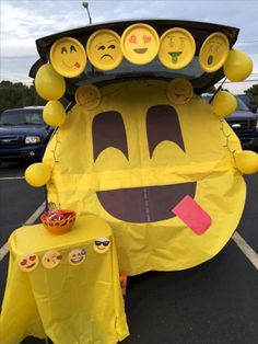 a large yellow car with many smiley faces on it's hood and some tables in the parking lot