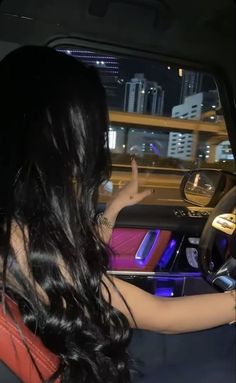 a woman driving a car at night with her hand on the steering wheel and she is wearing an orange top