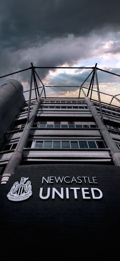 the new castle united logo is on the side of a tall building with dark clouds in the background