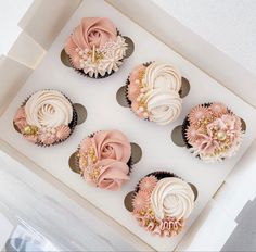 four cupcakes with pink and white frosting in a box on a table