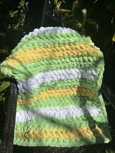 a green and yellow crocheted blanket sitting on top of a wooden chair next to a tree