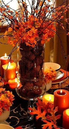 a vase filled with lots of orange flowers on top of a wooden table next to candles