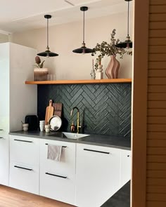 a kitchen with white cabinets and black backsplash, hanging lights above the sink