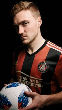 a young man holding a soccer ball in his hands and looking at the camera with an intense look on his face