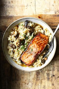 salmon and mushroom riso with rice in a bowl on a wooden table next to a fork