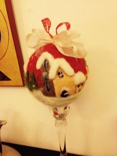 a wine glass with a christmas decoration on it sitting on a table next to a painting