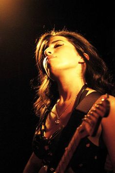 a woman singing into a microphone while holding a guitar in her hand and looking up at the sky