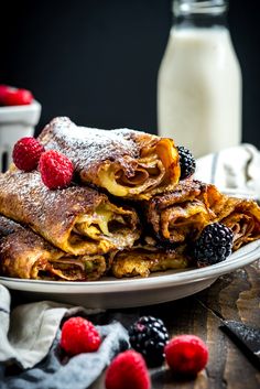 a stack of crepes on a plate with berries and powdered sugar next to it