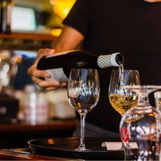 a person pouring wine into glasses on a bar