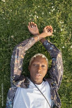 a woman laying in the grass with her hands above her head and looking at the camera