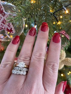 a woman's hand with two wedding rings on it and a christmas tree in the background