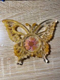 a yellow and pink butterfly brooch sitting on top of a wooden table next to a pair of scissors