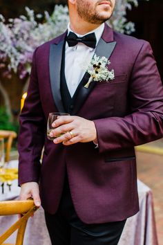 a man in a tuxedo standing next to a table with flowers and wine glasses