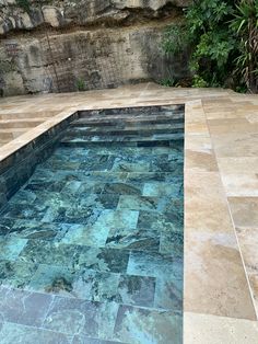 an empty swimming pool surrounded by rocks and greenery