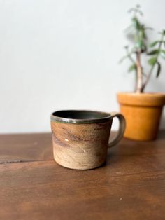 two ceramic cups sitting next to each other on top of a wooden table with a potted plant in the background