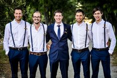 a group of men standing next to each other wearing blue suspenders and white shirts