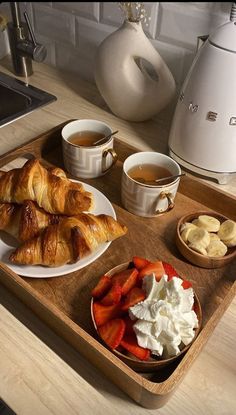 a wooden tray topped with croissants and fruit