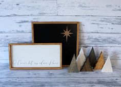 three wooden christmas trees in front of a framed sign