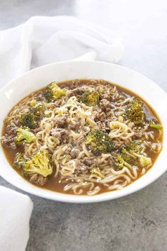 a white bowl filled with noodles and broccoli on top of a marble counter