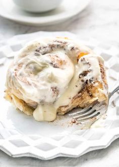 a close up of a fork on a plate with cinnamon rolls and cream cheese frosting