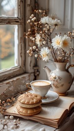 a cup of coffee and some cookies on a table near a vase with flowers in it