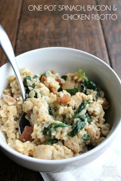 a white bowl filled with pasta and spinach on top of a wooden table next to a