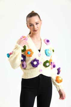 a woman in black pants and a white cardigan sweater with flowers on the sleeves