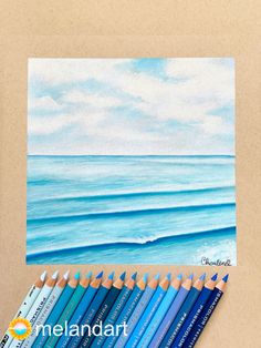 some colored pencils are next to an art project with the ocean in the background