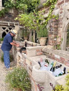 a man standing next to an outdoor grill with bottles and wine on the table in front of it