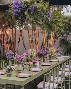 a long table is set with pink and purple flowers in vases, plates and place settings