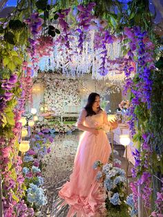 a woman in a pink dress is standing under a flower covered archway with candles and flowers all around her