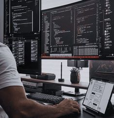 a man sitting at a desk in front of two computer monitors with screens on them