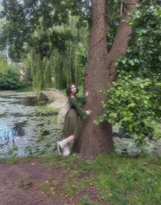 a woman in green dress standing next to a tree and holding onto a leafy branch