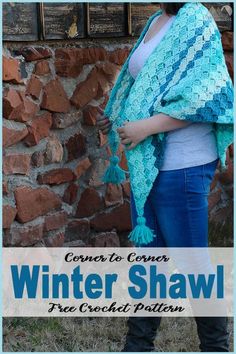 a woman standing in front of a brick wall wearing a blue crochet shawl