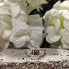 an engagement ring sitting on top of a stone block next to white hydrangeas