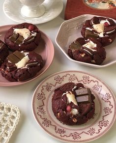 three plates with chocolate cookies on them next to a cup and saucer filled with marshmallows